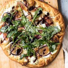 a pizza topped with greens and figs on top of a wooden cutting board