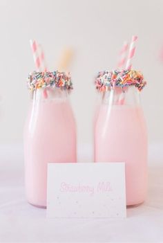 two pink milkshakes with strawberries and sprinkles on top are next to a card that says strawberry milk