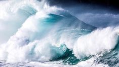 a large wave crashing into the ocean on a cloudy day