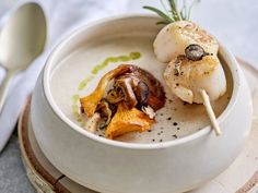 a white bowl filled with food on top of a wooden plate next to a spoon