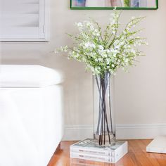 a vase filled with white flowers sitting on top of a book next to a painting