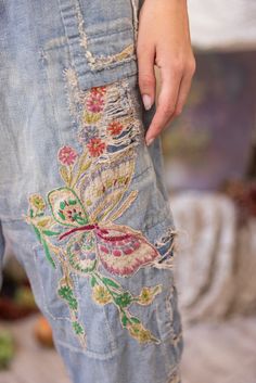 a person wearing jeans with embroidered flowers on the bottom and side, holding their hand in his pocket