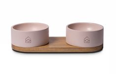 two pink bowls sitting on top of a wooden tray next to each other, one with a house symbol