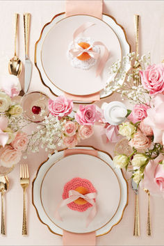 the table is set with pink flowers and white plates, gold cutlery and silverware