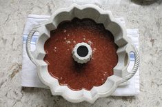 a cake pan filled with red sauce on top of a counter next to a white towel