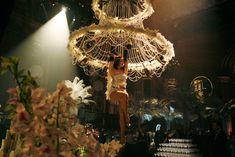 a woman standing on top of a table under a chandelier in a room filled with flowers