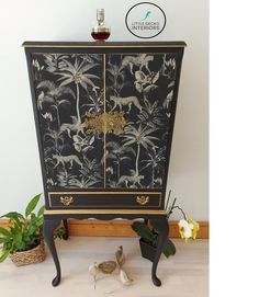 a black and gold painted cabinet with flowers on it