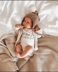 a baby doll that is laying down on a bed wearing a knitted hat and sweater