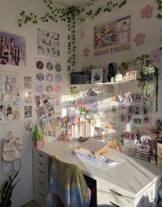 a white desk topped with lots of clutter next to a wall covered in pictures