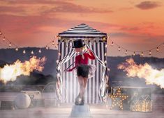 a woman standing on top of a white and black striped structure with fire in the air