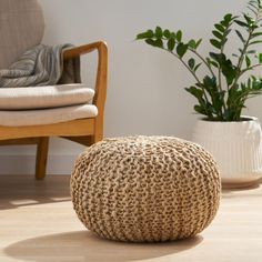 a large round woven poufce sits on the floor next to a chair and potted plant