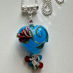 This is a small pendant created with an opal blue lampwork heart bead made by Jolene Wolfe in the UK.  There is a beautiful flower design on one side of the lampwork bead.  I accented it with 3 and 4 mm Swarovski caribbean opal, siam, and erinite bicone crystals, sterling bead caps, and tiny sterling spacer beads.  The sterling bail has a lovely little flower in the middle of it to continue the floral theme.  The pendant itself measures 2 inches from the top of the bail to the bottom of the dang Beautiful Flower Designs, Floral Theme, Small Pendant, Valentines Gift, Heart Beads, Bead Caps, Lampwork Beads, Beautiful Flower, Blue Opal