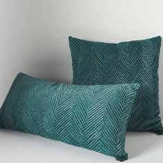 two green pillows sitting next to each other on top of a white surface with one pillow in the shape of a herringbone pattern