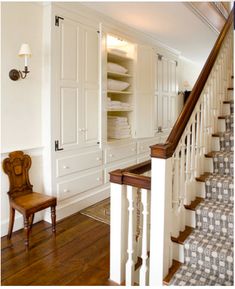 a room with some stairs and white cabinets in the corner, next to a wooden chair