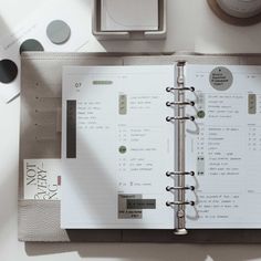 an open planner sitting on top of a desk next to a clock and other items