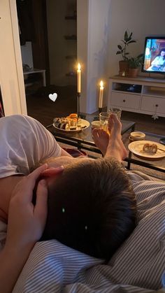 a person laying in bed with food on the table next to him and a candle