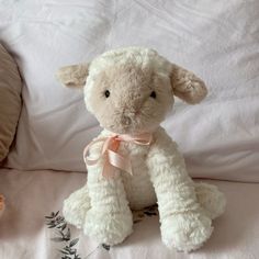 a white stuffed lamb sitting on top of a bed next to a teddy bear with a pink bow