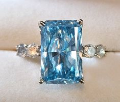 Gorgeous brilliant cut 8.59ct lab grown blue diamond ring bookended by .8ctw natural diamonds. Center lab grown diamond: Cut Cornered Rectangular Modified Brilliant 15.74x10.2x6.01mm SI1-SI2 Clarity Side natural diamonds: round brilliant cut 3.8 mm approximate .8ctw color H-J clarity I1-I2 Ring: 14ct white gold out of roundGorgeous brilliant cut 8.59ct lab grown blue diamond ring bookended by .8ctw natural diamonds. Center lab grown diamond: Cut Cornered Rectangular Modified Brilliant 15.74x10.2 Luxury Blue Radiant Cut Diamond Ring, Blue Radiant Cut Diamond Accented Jewelry, Dazzling Blue Diamond Cut Ring, Blue Moissanite Jewelry With Diamond Accents, Blue Asscher Cut Diamond Ring With Accents, Blue Diamond Ring With Diamond Accents Emerald Cut, Blue Radiant Cut Diamond Jewelry, Blue Emerald Cut Diamond Ring With Diamond Accents, Blue Emerald Cut Diamond Ring With Accents