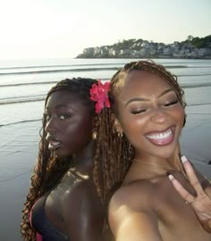 two beautiful women standing next to each other near the ocean with their fingers in the air