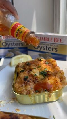 a person is pouring sauce onto a casserole on a plate with lemon wedges