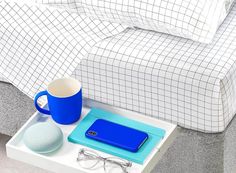 a table with a laptop, eyeglasses and a cup on it next to a bed