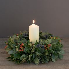 a white candle is lit on top of a wreath with greenery and red berries