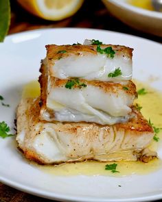 two pieces of fish sitting on top of a white plate next to lemon wedges