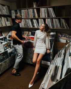 a man standing next to a woman in front of a record shelf filled with records