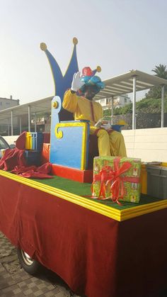 a man dressed as a clown riding on the back of a truck filled with presents