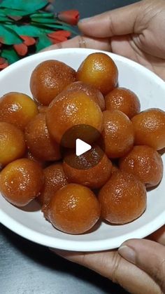 a person holding a white bowl filled with small oranges on top of a table