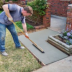 a man with a mop is laying cement on the ground in front of his house