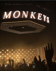 a crowd of people at a concert with their hands in the air and lights above them