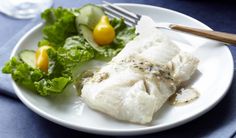 a white plate topped with fish next to a green leafy salad on a blue table cloth