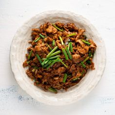 a white bowl filled with meat and green onions