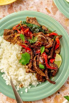 a green plate topped with meat and rice next to a fork on top of a table