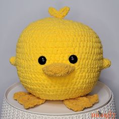 a crocheted yellow stuffed bird sitting on top of a white stand with black eyes