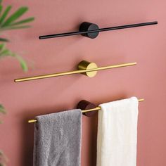 two towels hanging on the wall next to a towel rack and toilet paper roll in front of a pink wall