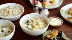 four bowls of soup are sitting on a table with spoons and other food items