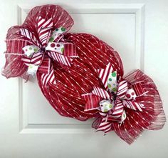 a red and white wreath hanging on the front door with ribbons tied around it's sides