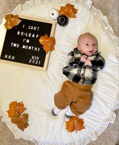 a baby laying on top of a white blanket next to a sign that says i can't be leaf i'm two months now