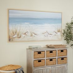 a painting hangs on the wall next to a dresser with baskets in front of it