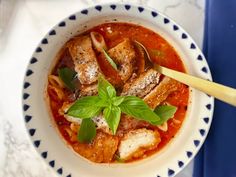 a bowl filled with meat and tomato soup on top of a blue and white table