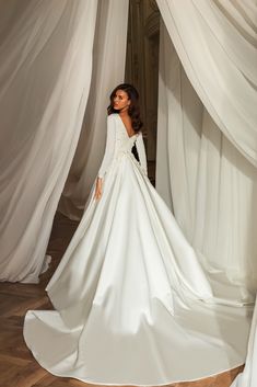 a woman in a white wedding dress standing next to some drapes and looking off into the distance