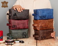 a man holding four different colored bags on top of a wooden table next to other items