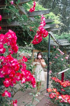 a woman wearing a face mask standing in front of some pink flowers and greenery