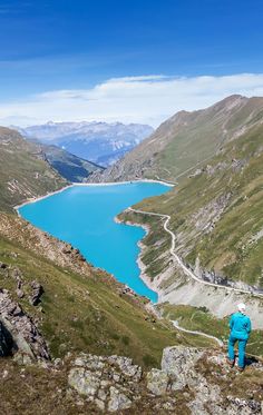 a man standing on top of a mountain next to a blue lake in the mountains