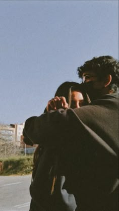 a man and woman standing next to each other on the side of the road looking at their cell phones