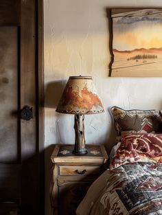 a bed sitting next to a lamp on top of a wooden dresser under a painting