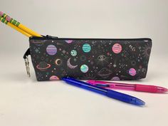 two pencils and a pen sitting next to a black bag with planets on it