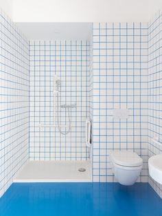 a white toilet sitting next to a shower in a blue tiled bathroom with tile walls